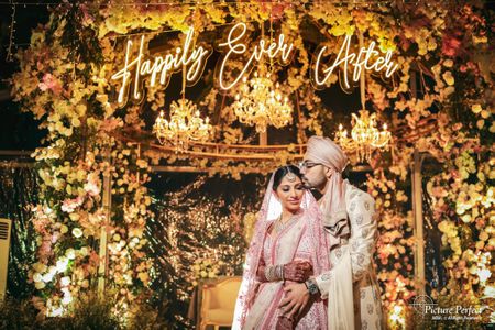 A candid shot of the couple in pastel outfits with Happily Ever After backdrop.
