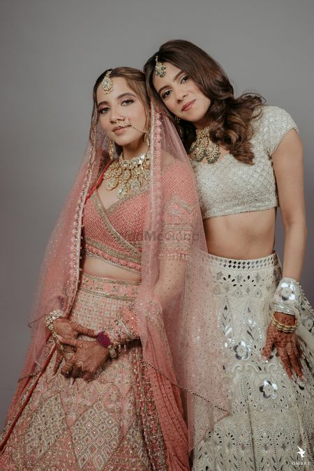 Photo of bride in peach with her sister in an ivory lehenga