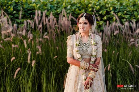 A bride in an ivory and gold lehenga with pastel jaimala 