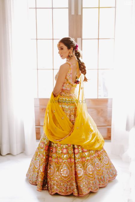 heavy yellow lehenga with braided hairstyles and floral wreath