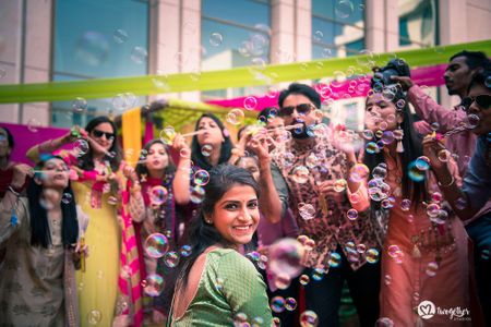 Cute mehendi photo of bride with bridesmaids blowing bubbles