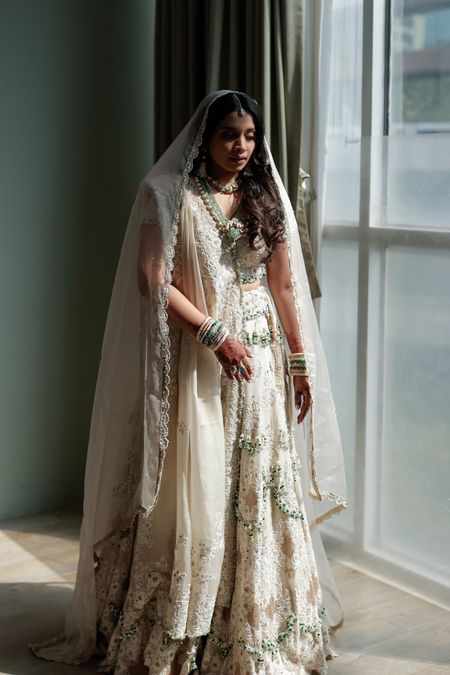 Solo bridal portrait with bride dazzling in an all-ivory lehenga and layered jewellery