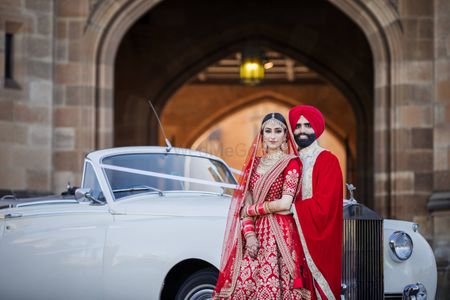 A color-coordinated couple posing on their wedding day in front of vintage car.