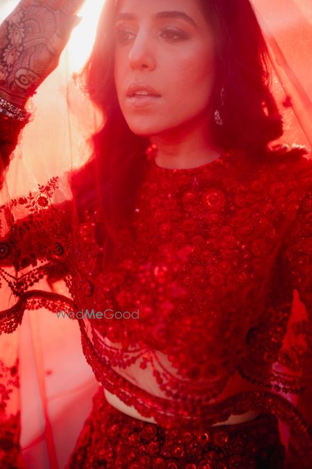 Bride under a sheer veil in a deep red lehenga with monotone embrodiery 