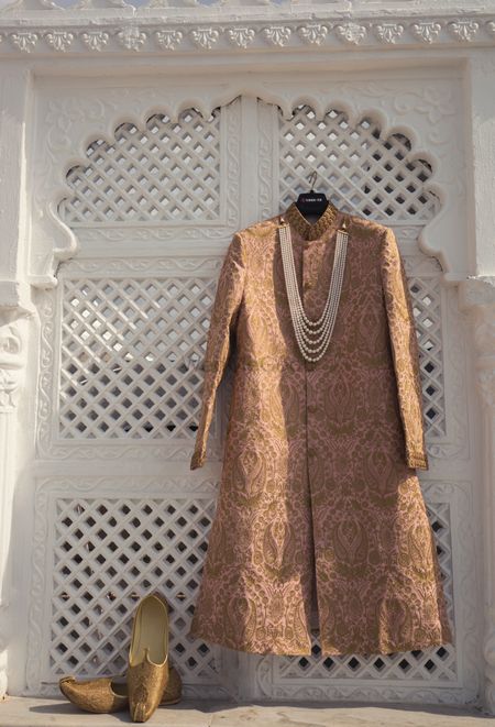 Photo of Brown sherwani on hanger with groom jewellery