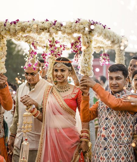 Bride entering under phoolon ki chadar in red lehenga 