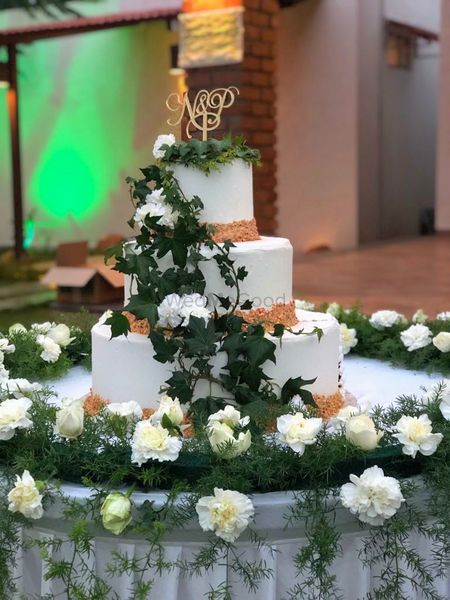 Photo of Three-tiered wedding cake with foliage and flowers.