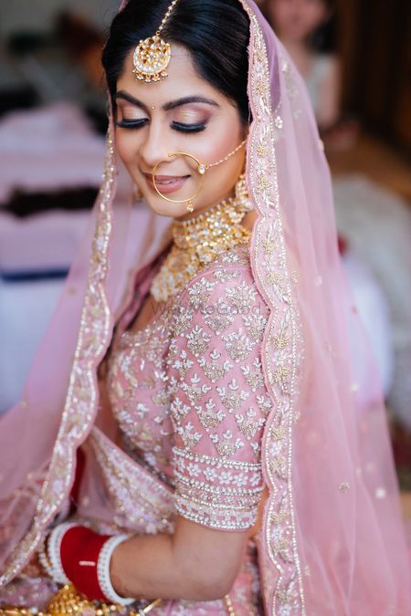 Bride wearing pink lehenga with contrasting jewellery.