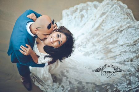 Romantic beach shot of groom kissing bride in lace gown after marriage