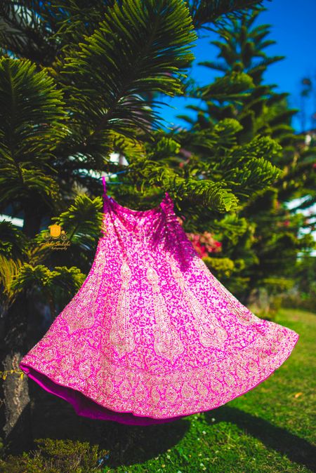 Photo of Beautiful pink and gold lehenga hanging on a tree