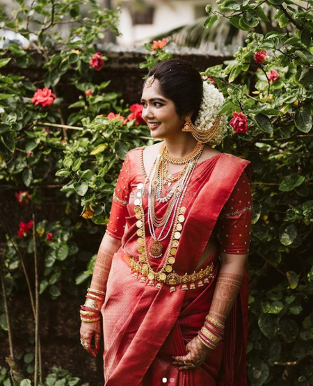 South Indian bride in a brick red saree with contrasting jewellery.