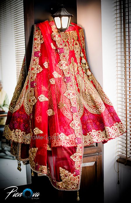 Photo of Red and gold bridal lehenga on hanger in room