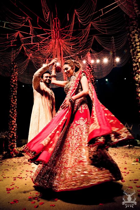 Photo of bride in red bridal lehenga spinning around groom