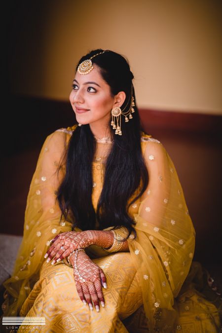 A bride in a gold mehendi outfit with waterfall earrings