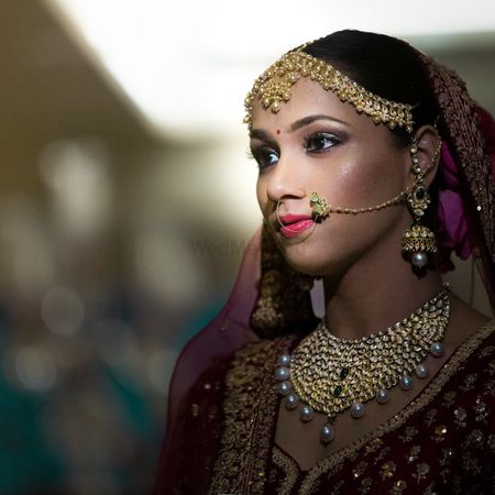 A bride in a maroon outfit and gold jewelry