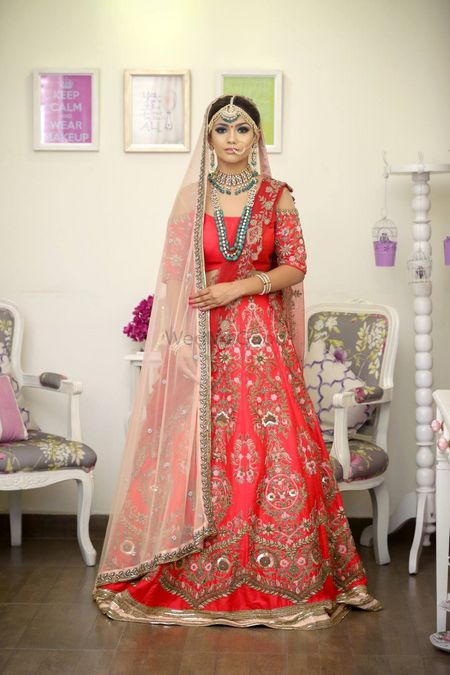 Photo of Bride in red and gold cold shoulder lehenga with green jewellery