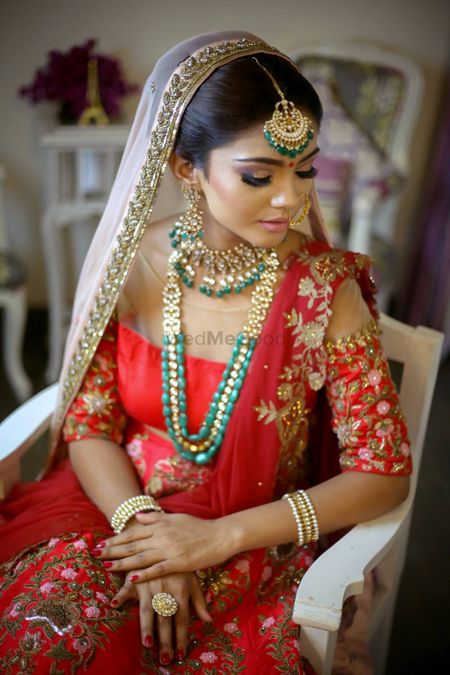 Bride in red and gold bridal outfit with green jewellery and cold shoulder