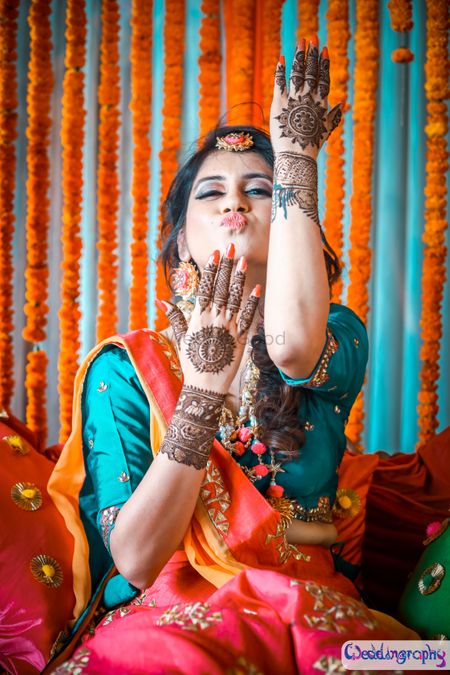Bride showing off mehendi with orange and teal backdrop