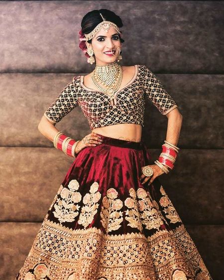 A bride in a maroon lehenga poses for the camera

