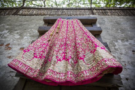 Bright pink lehenga with unique gold embroidery on hanger