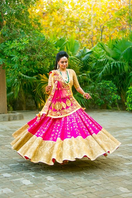 Photo of Bride twirling in gold and pink lehenga with broad border