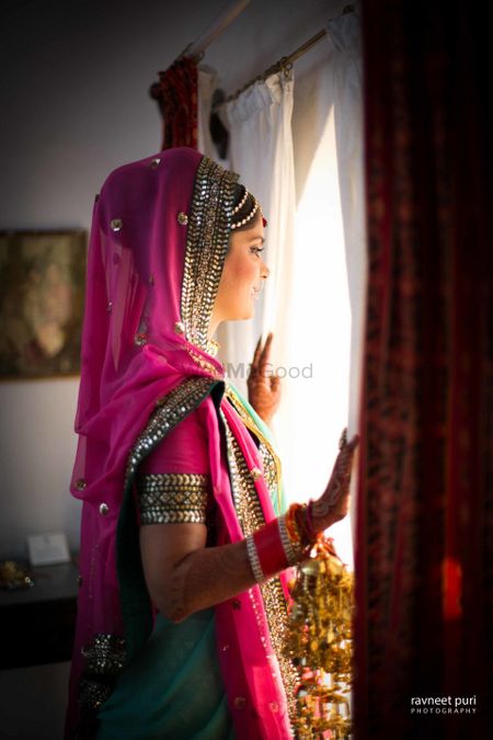 Bride in green and pink bridal lehenga looking out of window