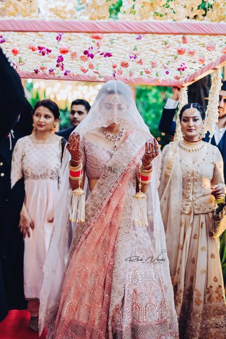 Photo of A bride in a soft pink lehenga and a veil entering with her brothers and sisters