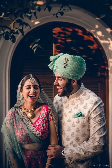 Photo of A bride and groom in color-coordinated outfits laughing on their wedding day