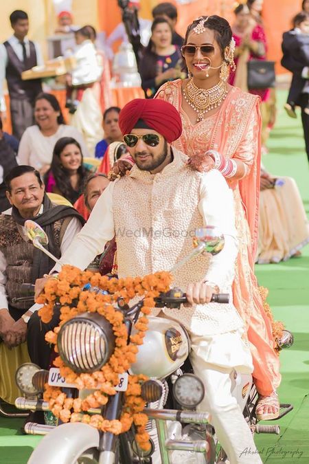 A sikh bride and groom enter the wedding venue on a bike