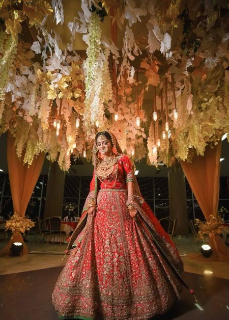 A bride in red poses under a ceiling of flowers