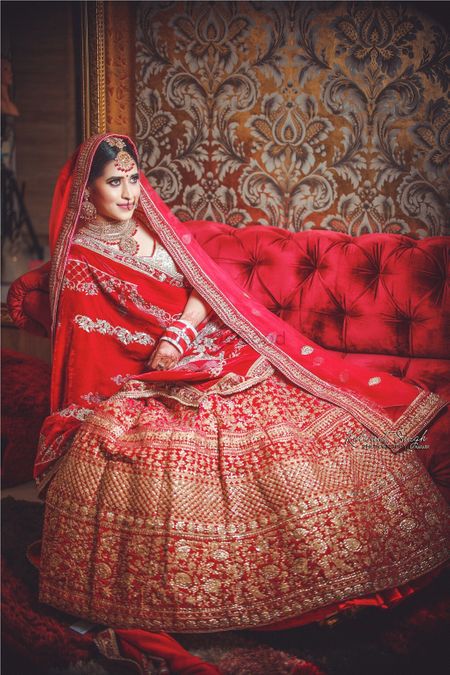 Bride sitting on sofa in bright red and gold lehenga 