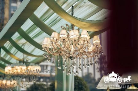 Photo of Lovely white and gold crystal chandelier on a draped ceiling in moss green for a wedding event