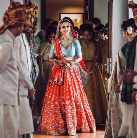 A bride in a tomato red lehenga with a contrasting blue blouse