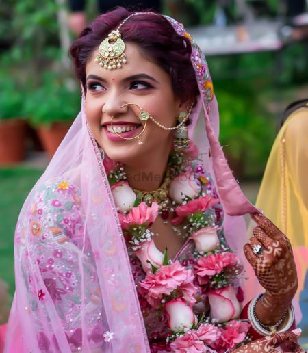 Candid shot of a bride wearing pink lehenga with green enameled jewellery.