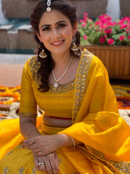 A bride in a yellow outfit and nude makeup for her mehndi ceremony