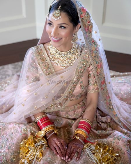 Photo of Bride in a light pink and gold lehenga with kaleere