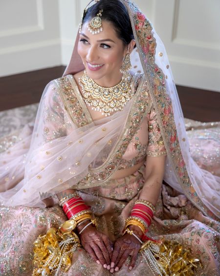 Photo of Bride in a light pink and gold lehenga with kaleere