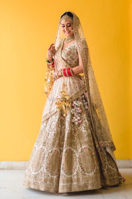 A bride in a beige lehenga with intricate golden embroidery