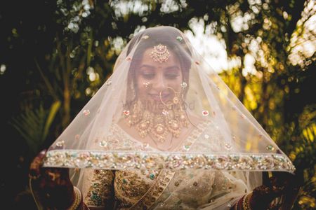 bride holding her gold and ivory dupatta as veil