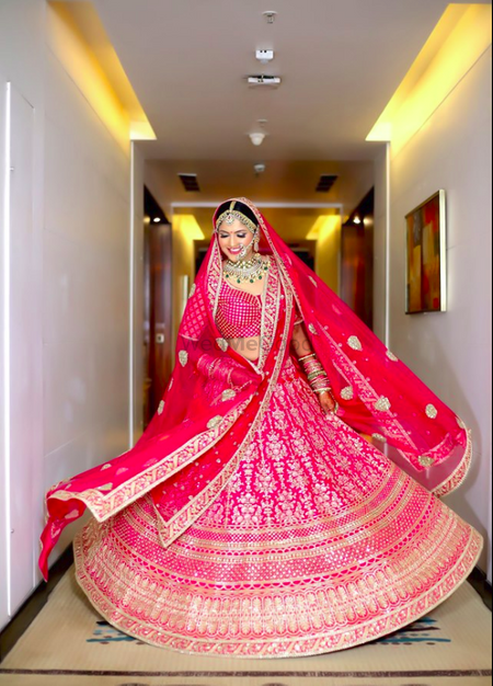Photo of A bride in a pink and red lehenga twirling on her wedding day