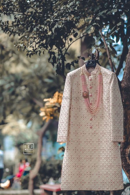 A white and pink textured sherwani with a pink beaded mala.