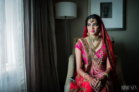 Photo of Bride in neon pink lehenga wearing layered necklace