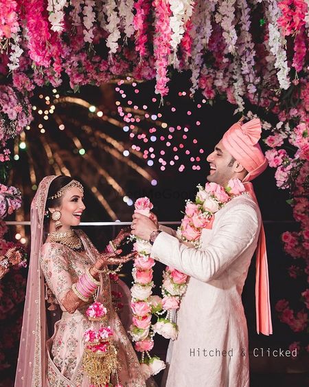Photo of fun couple shot holding rose jaimalas and wearing pastels