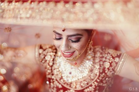 bride in red and gold holding her dupatta as veil shot