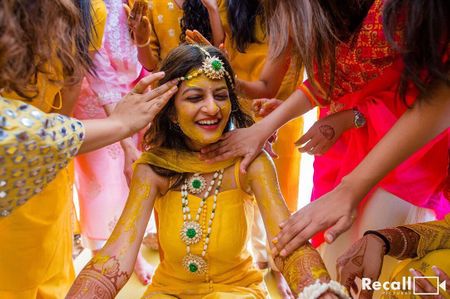 Photo of fun haldi bridal portrait with everyone putting it on her