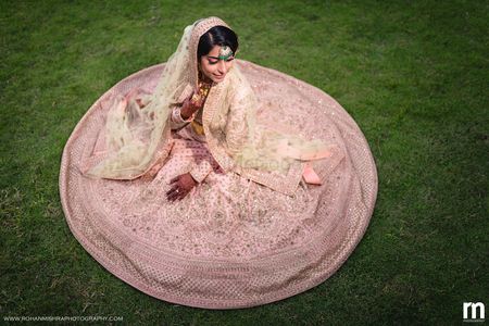 Bride sitting with pastel pink lehenga flared out 