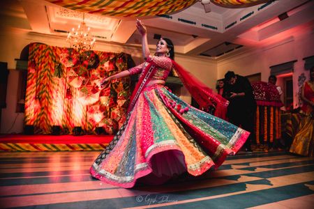 A bride in a multicolored lehenga dancing on her mehendi 