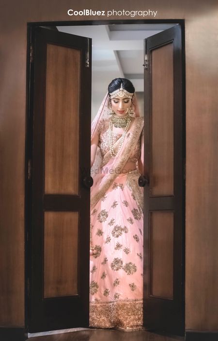 Bride entering through door in light pink and gold lehenga
