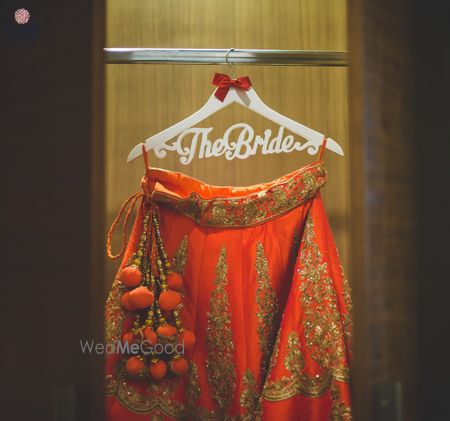 Photo of Red and gold lehenga hanging on customised bridal hanger