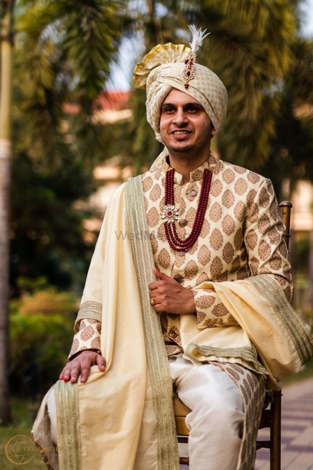 A happy portrait of a groom dressed in a classic white & gold sherwani